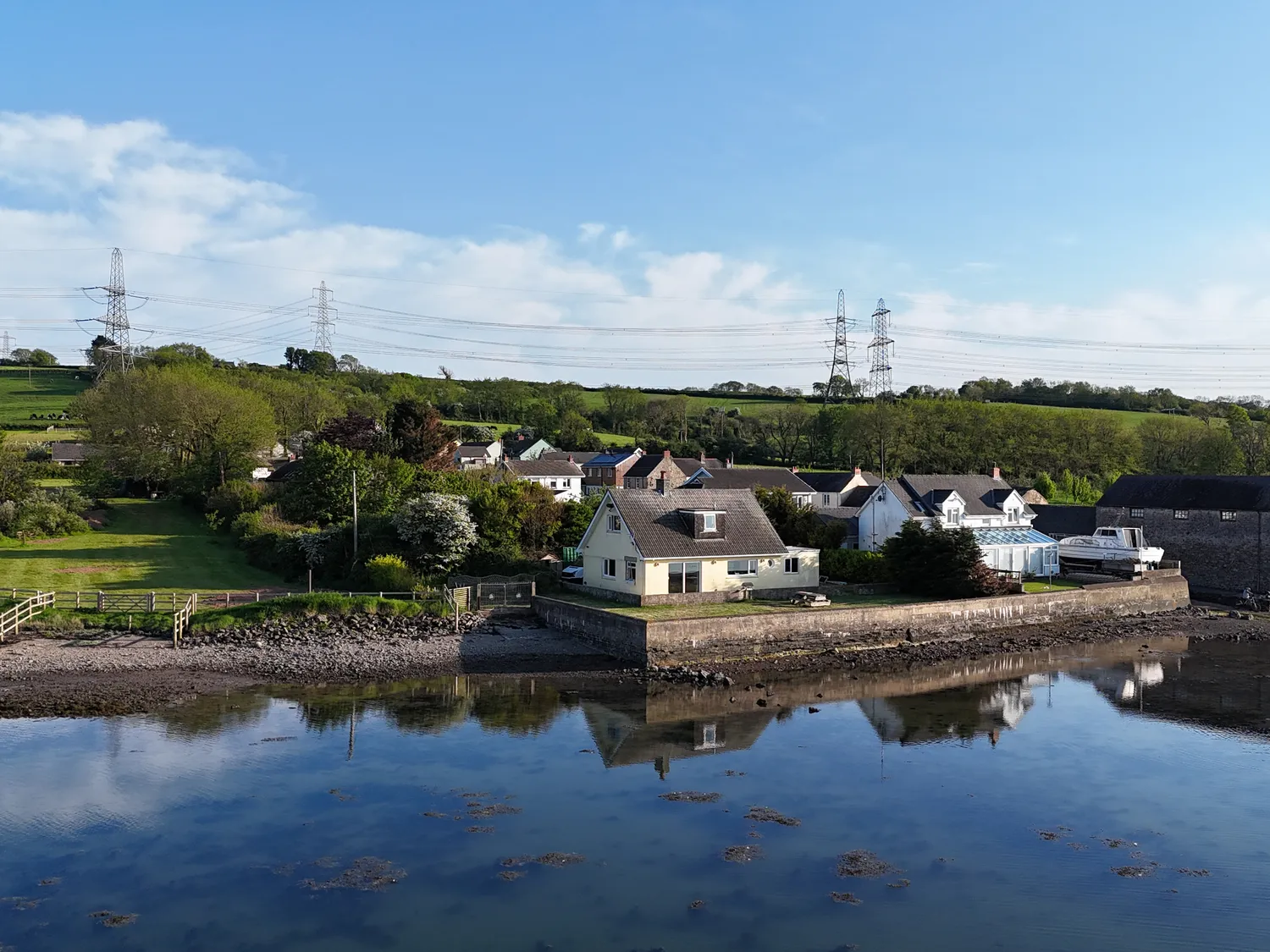Shearwater Cottage from above the river on a clear sunny day, with other cottages behind it.